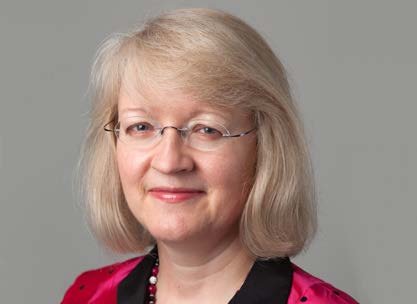 Portrait of a woman with blonde hair and glasses, wearing a pink top and a beaded necklace.
