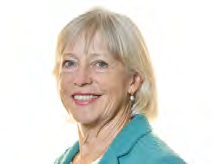 Headshot of an older woman with blonde hair, smiling, wearing a teal jacket and pearl earrings.