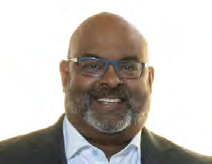 Headshot of a Black man with a beard and blue-rimmed glasses, smiling broadly.