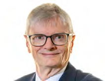 Headshot of an older man with gray hair and glasses, smiling, in a dark suit.