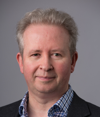 Headshot of a white male with gray hair, wearing a checkered blue shirt and dark jacket.