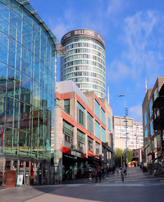 Street scene in Birmingham showing modern architecture including the glass Selfridges building on the left and the Bullring tower in the background, with people walking on the pavement.