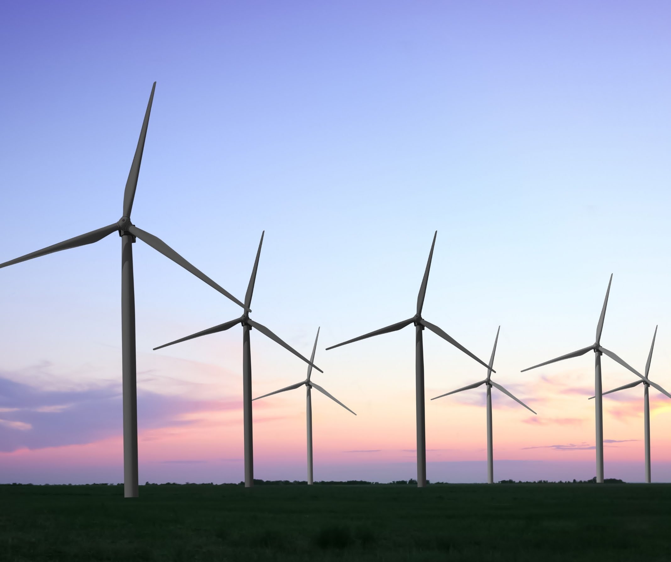 A row of wind turbines in a green field against a sunset sky with blue, purple, and pink hues.