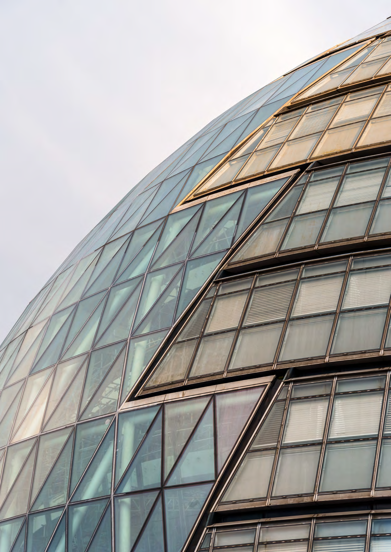 Close-up of a modern glass building facade with many triangular and rectangular panels, some angled open.