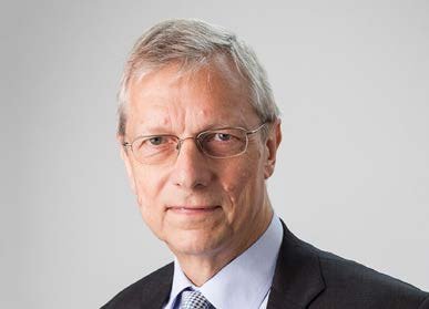 Headshot of an older man with grey hair and glasses, wearing a dark suit and patterned tie.