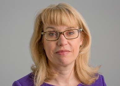 Headshot of a woman with blonde hair and glasses, wearing a purple top.