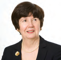 Headshot of an older woman with short brown hair, wearing a black suit and pearl necklace, smiling.