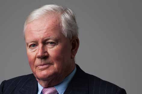 Headshot of an older white man with white hair, wearing a suit and pink tie.