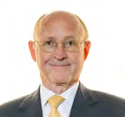 Headshot of an older man with glasses, wearing a suit and yellow tie, smiling.