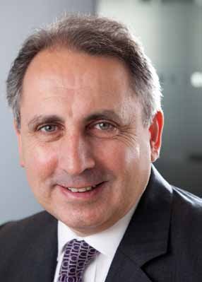 Portrait of a man with short dark hair, smiling and wearing a suit and patterned tie.