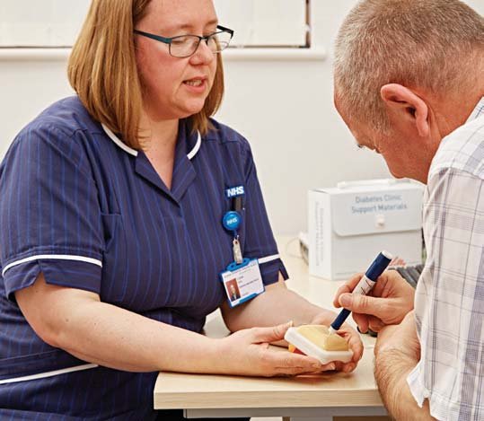 Nurse demonstrating insulin injection technique on a model arm to a patient, emphasizing medical education.