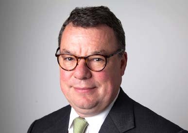 Headshot of a man with glasses, wearing a dark suit and green patterned tie.