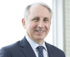 Headshot of a smiling man with graying hair, wearing a dark suit and patterned blue tie.