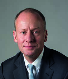 Portrait of a bald man in a dark suit and light blue patterned tie.