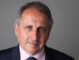 Portrait of a man with graying hair, wearing a suit and pink shirt with a patterned tie, looking directly at the viewer.